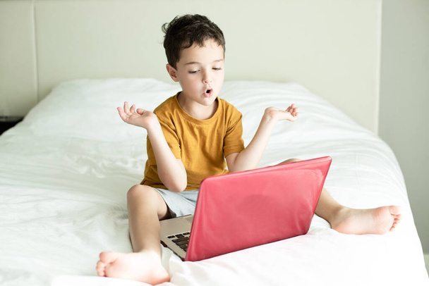 Distance learning concept, modern education technologies, online language courses. Preschool lesson in white bedroom with a laptop. Happy child gestures, mouth makes sounds. Emotional face. Caucasian - Photo, Image