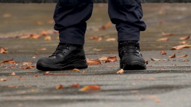Herbst. Details. Militärstiefel an den Füßen des Mannes. Polizisten vor die Füße. Stiefel von Polizisten in Uniform. Beine eines Polizisten aus nächster Nähe im Dienst. Füße eines Wachmannes in schwarzen Stiefeln. Gefallene Blätter - Filmmaterial, Video