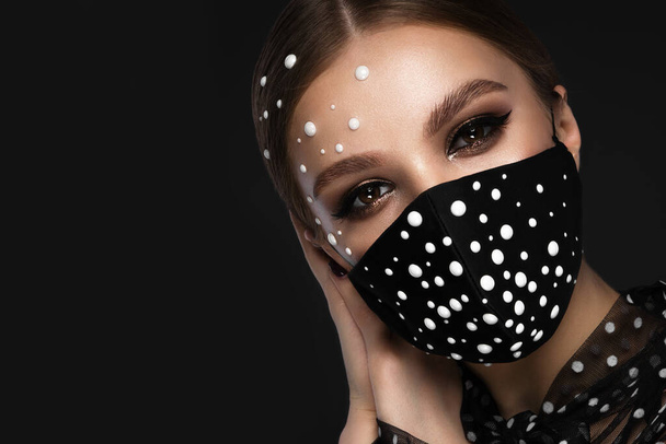 Portret van een mooie vrouw in een zwart masker met parels en klassieke make-up. Maskermodus tijdens de hevige pandemie - Foto, afbeelding