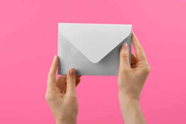 Женщина держит белый бумажный конверт на розовом фоне, крупным планом - Фото, изображение