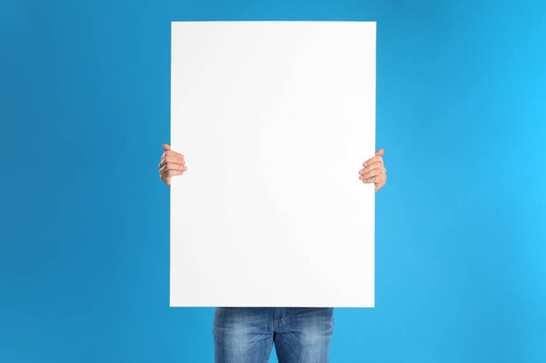 Man holding blank poster on blue background - Foto, imagen