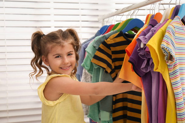 Little girl choosing clothes on rack indoors - Foto, imagen