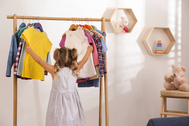 Little girl choosing clothes on rack in room - Fotó, kép