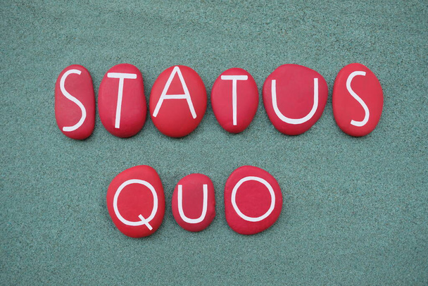 Status Quo, латинская фраза, написанная красными буквами из камня на зеленом песке - Фото, изображение