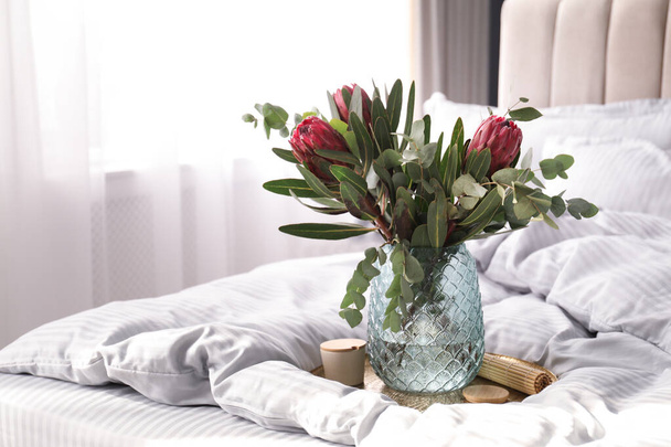Vase with bouquet of beautiful Protea flowers on bed indoors - Foto, Bild