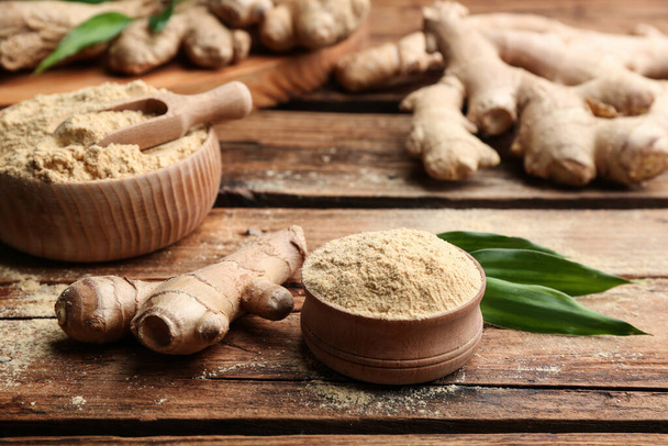Dry ginger powder, fresh root and leaves on wooden table - 写真・画像