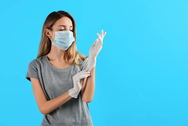 Young woman in protective mask putting on medical gloves against light blue background. Space for text - Foto, Bild