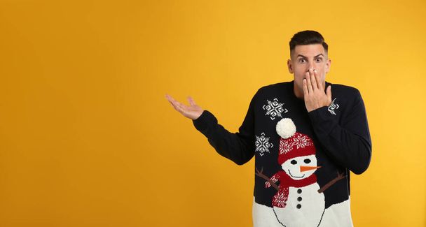 Shocked man in Christmas sweater on yellow background - Zdjęcie, obraz