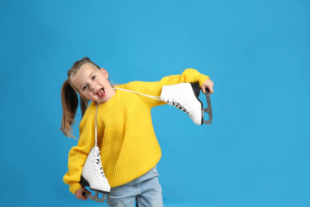 Excited little girl in yellow knitted sweater with ice skates on blue background - Foto, immagini