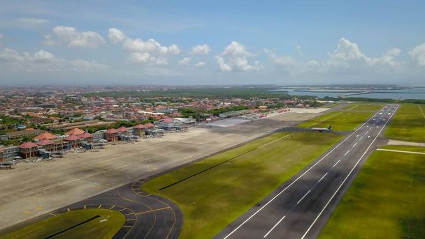 Letiště - letecký výhled s přistávacími drahami, taxi, trávou a letadly. Letecký výhled na letiště Ngurah Rai. Letadlo letí po ranveji - Fotografie, Obrázek
