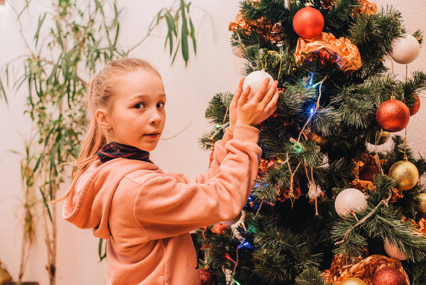 Μικρό κοριτσάκι κοντά στο χριστουγεννιάτικο δέντρο στο σπίτι. Χριστουγεννιάτικο δέντρο εφήβων κοριτσιών. - Φωτογραφία, εικόνα