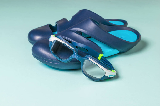 Brillen en teenslippers voor het zwembad op een blauwe achtergrond. - Foto, afbeelding