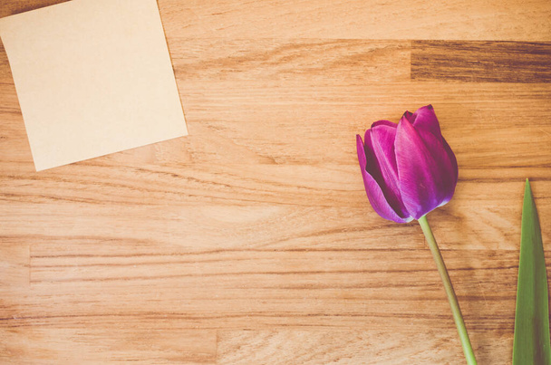 A high angle shot of a purple tulip and a piece of paper on a wooden surface - copy space - Foto, afbeelding