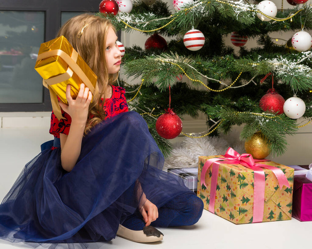 Lovely Girl Sitting on Floor in Front of Christmas Tree with Gift Box. - Φωτογραφία, εικόνα