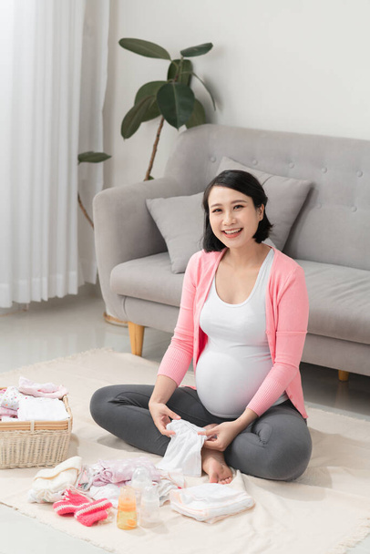 aziatische moeder voorbereiding weinig kleding voor nieuwe baby wanneer zitten op de vloer - Foto, afbeelding