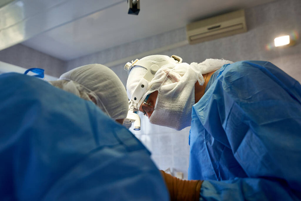 Chirurgie. Un chirurgien dans la lampe frontale en uniforme bleu effectue une opération. Intervention médicale. - Photo, image