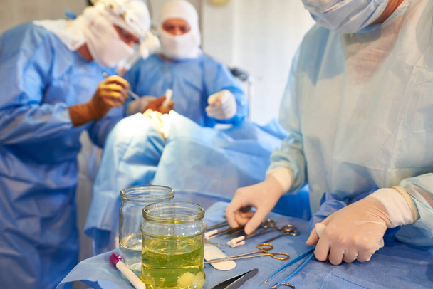 Cirugía. En primer plano hay una mesa con instrumentos, en segundo plano, los cirujanos están realizando una operación. - Foto, Imagen