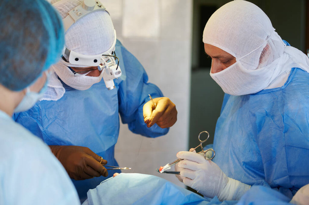 Surgery. Team of surgeons in blue suits stitch up the wound. - Photo, Image