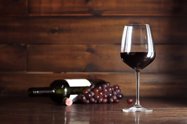 Copo de vinho tinto e garrafa e uvas vermelhas em fundo de madeira - Foto, Imagem