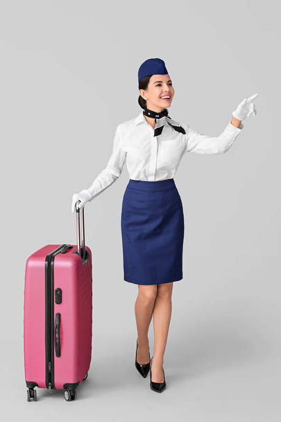 Beautiful stewardess with luggage on grey background - Foto, afbeelding