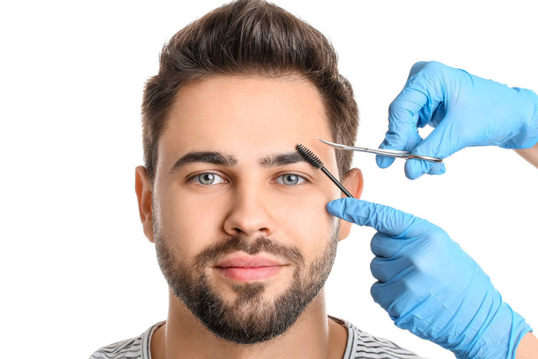 Jeune homme subissant une procédure de correction des sourcils sur fond blanc - Photo, image