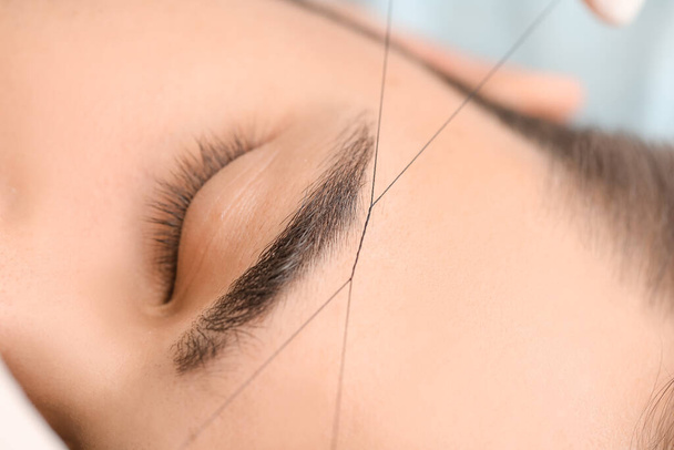 Young man undergoing eyebrow correction procedure in beauty salon, closeup - Fotó, kép