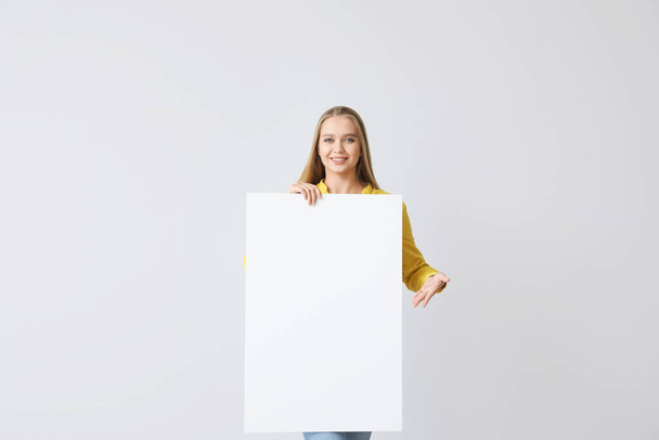 Beautiful young woman with blank poster on grey background - Photo, Image