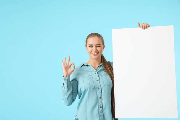 Beautiful young woman with blank poster showing OK on color background - Photo, Image