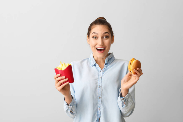 Happy young woman with french fries and burger on light background - Photo, Image