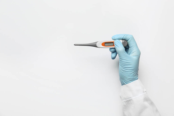 Hand van arts met thermometer op lichte achtergrond - Foto, afbeelding