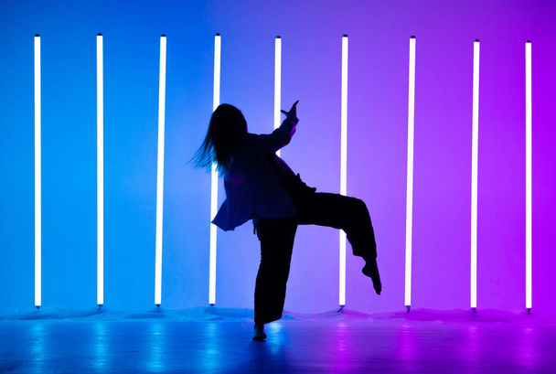 Attractive young woman dancer dancing contemporary in the studio on a blue purple background with neon lighting lamp. - Valokuva, kuva