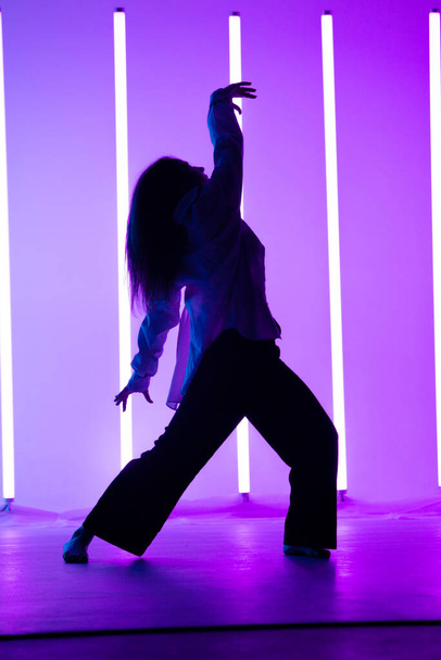 Attractive young woman dancer dancing contemporary in the studio on a blue purple background with neon lighting lamp. - Foto, immagini