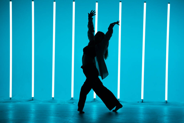 Pretty young woman dancer in a youth fashion streetwear dancing contemporary in the studio on a colorful background with neon lighting tube in disco style. Dance color poster. - Foto, Imagen