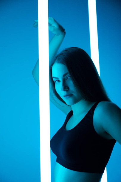 Portrait of modern young woman dancer posing in the studio on a colorful background with neon lighting tube. - Fotó, kép