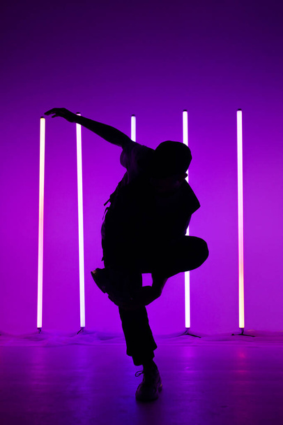 Portrait of handsome person doing hip hop elements on neon lamps purple lights background. Close up man dancing at party in night club. Silhouette. Dance school poster. - Фото, изображение
