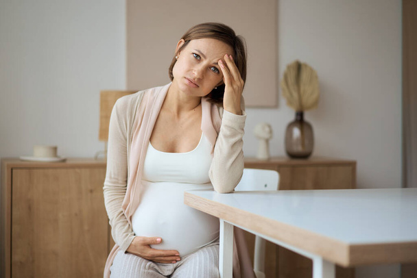 Donna incinta che soffre di mal di testa mentre è seduta a tavola - Foto, immagini