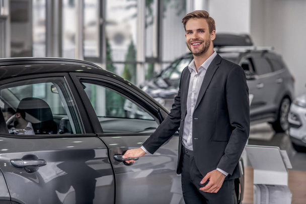 Smilng male opening car door in the showroom - Photo, Image