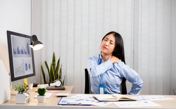 アジアの女性会計士は椅子で仕事をするのに疲れ、オフィスで一生懸命仕事をしながらリラックスしてリラックスしています. - 写真・画像