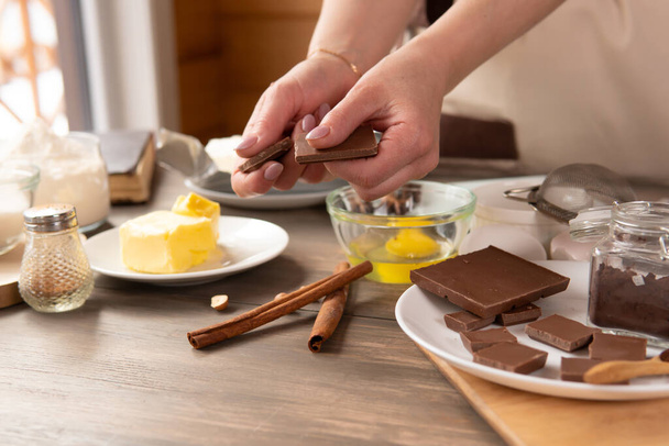 Beautiful woman prepares dessert in the kitchen of the house for her family. She's holding chocolate - Foto, afbeelding