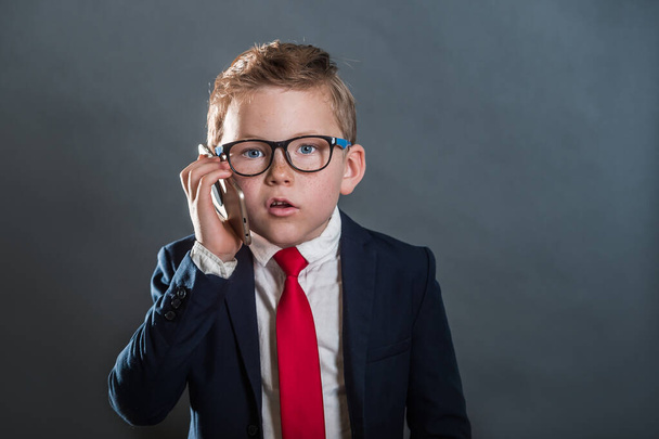 Back to school. Kid businessman. Confident little pupil in suit and phone in hand. Child talking on smartphone. Leader. Boy dressed as businessman talking on the phone isolated on grey background. - Φωτογραφία, εικόνα