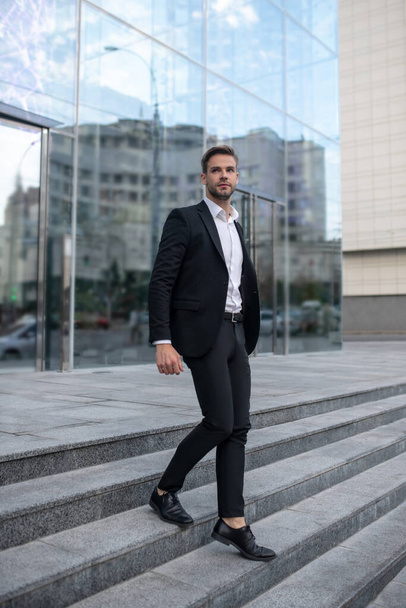Stylish young man in a black suit on the steps - Foto, Bild