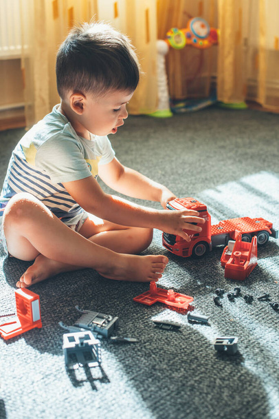 Foto vista lateral de un chico caucásico jugando en el suelo con bloques de coches y constructores - Foto, Imagen