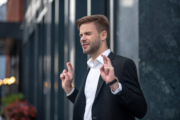 Young businessman looking excited keeping fingers crossed - 写真・画像