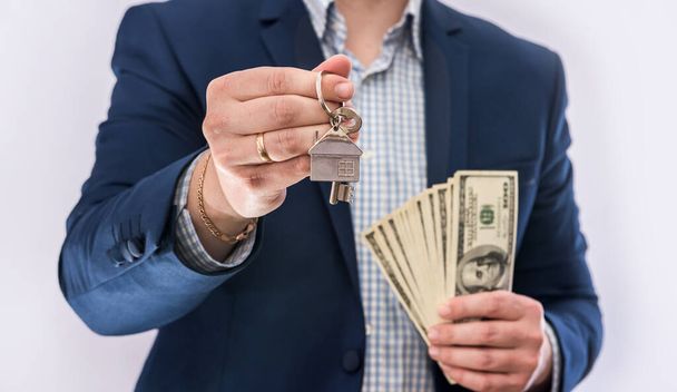 Mannelijke handen met Amerikaanse dollars biljetten en huissleutel geïsoleerd. Conceptkoop of vastgoedlening  - Foto, afbeelding
