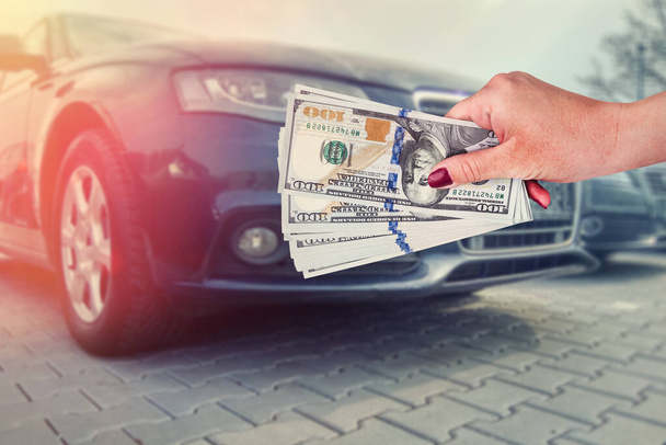продавец, продающий авто в автомагазине или бизнесмен, покупающий новый автомобиль, держа в руках доллар. - Фото, изображение