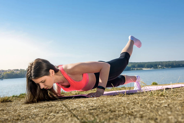 young athletic woman doing push ups. Girl doing fitness exercises near the lake at daytime - Foto, imagen