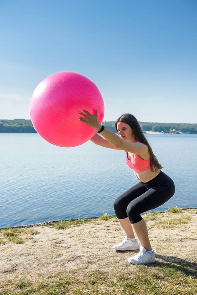 Νεαρή γυναίκα σε φόρμα στα αθλητικά κατά τη διάρκεια της γυμναστικής και την άσκηση με μπάλα στη λίμνη. Υγιής τρόπος ζωής - Φωτογραφία, εικόνα