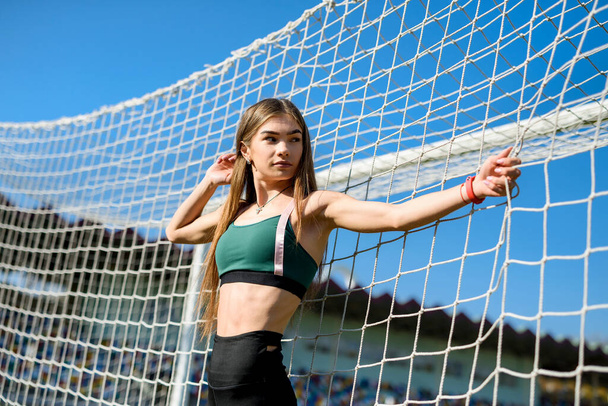Een mooi meisje met een perfect figuur staat vlak bij een voetbaldoelpunt in het stadion. Fitness en gezond lifestyle concept. - Foto, afbeelding
