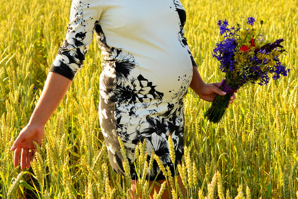 έγκυος γυναίκα με λουλούδια αγκαλιάζει την κοιλιά με τα χέρια σε εξωτερικούς χώρους - Φωτογραφία, εικόνα