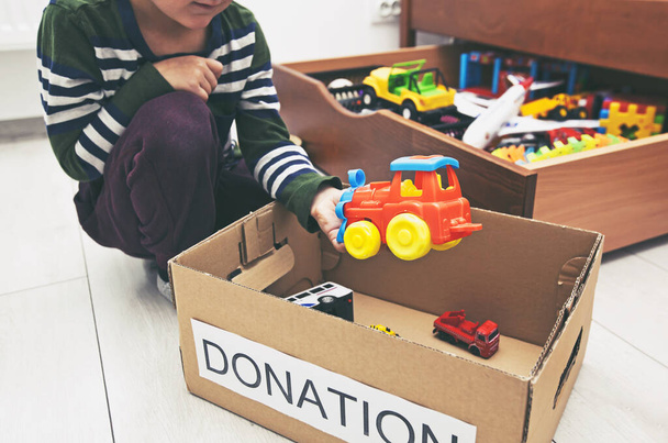 The boy is sorting his toys and puts toy car into the donation box - Foto, Imagen